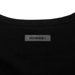 Close-up of a black garment with 'HOMME+' label on a white background